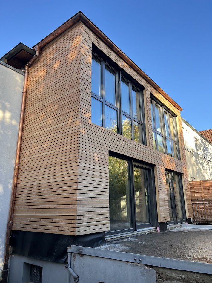 Anbau mit Holzfassade  Moderner Anbau mit klarer Formensprache und horizontaler Holzfassade. Große Fensterflächen sorgen für viel Tageslicht und eine offene, helle Atmosphäre. Die natürliche Holzverkleidung verbindet zeitgemäßes Design mit Nachhaltigkeit und fügt sich harmonisch in den Bestand ein.